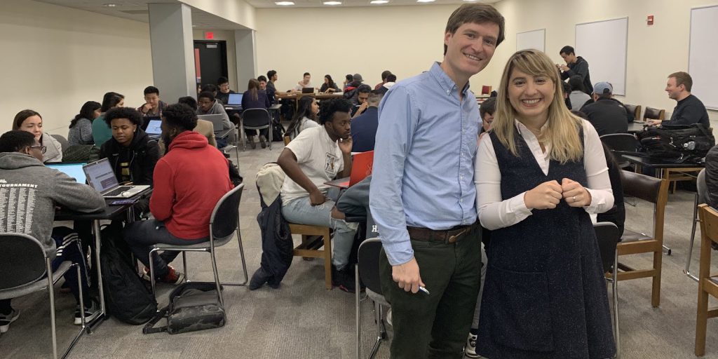 David Weintrop and Hernisa Kacorri standing looking at the camera with students sitting at tables behind them