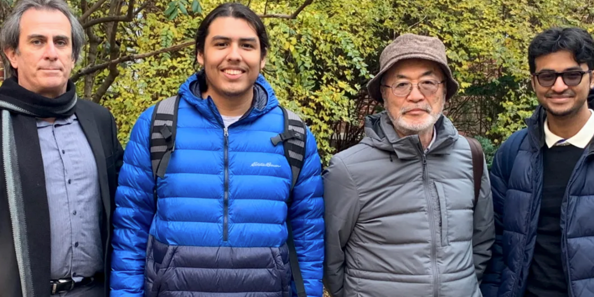 Professor Richard Marciano, and students Isaac Hernandez and Akif Zaman team stand next to Haruo Kawate. They are standing in front of green shrubbery on University of Maryland's campus