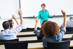 Students raising hands to ask question in lecture hall classroom