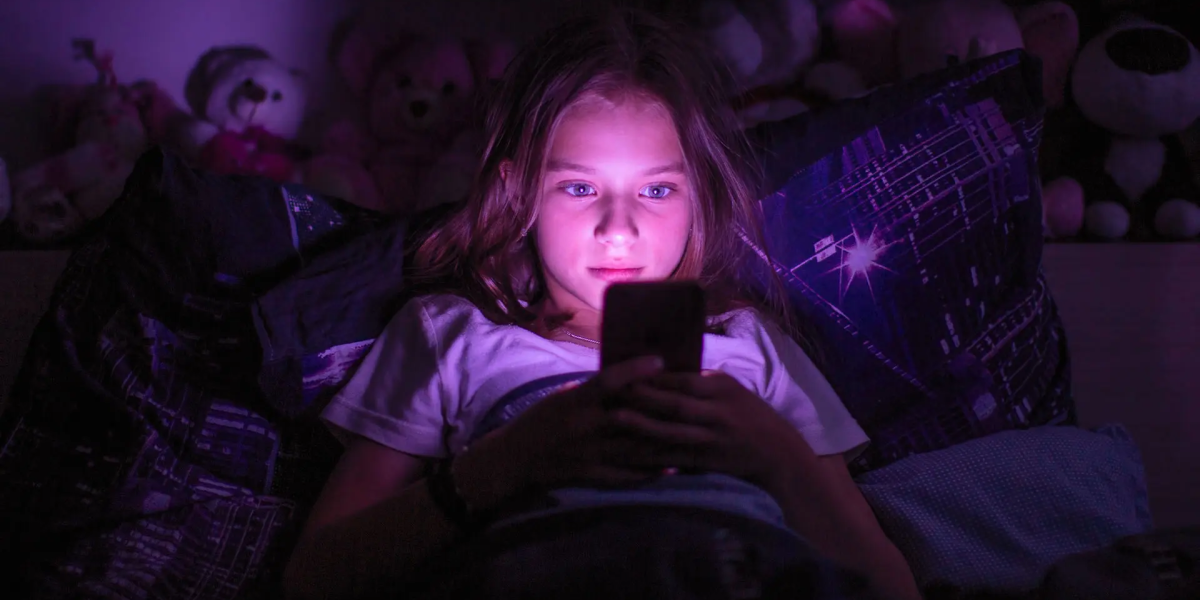 Image of a young girl in a dark room looking at her cell phone