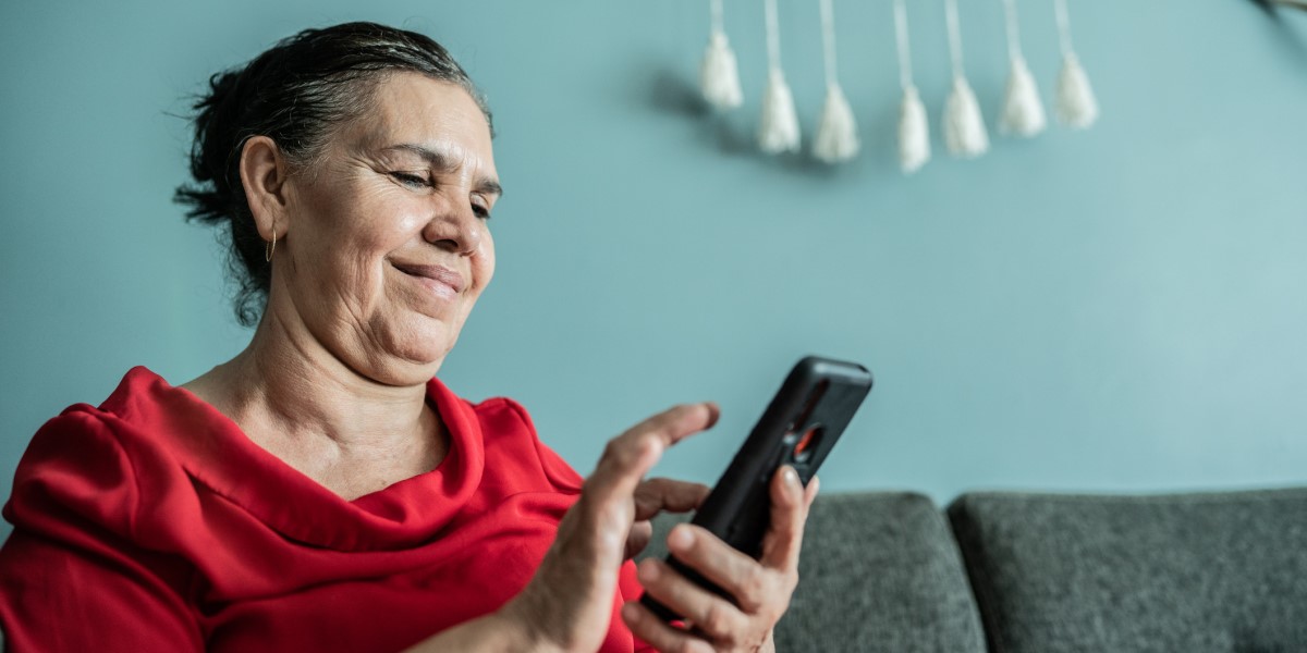Photo of a woman sitting on a couch and looking at a smart phone that she is holding.