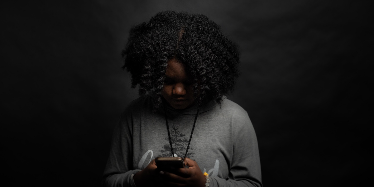 A black woman in a dark room looking down at a smartphone