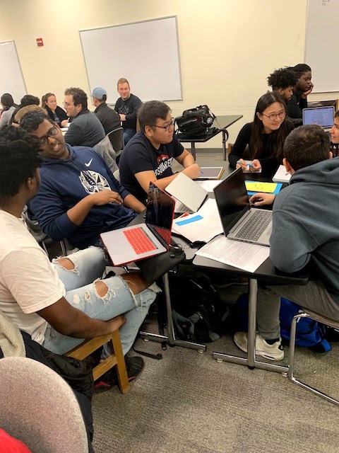 people sitting around a table with laptops talking to one another