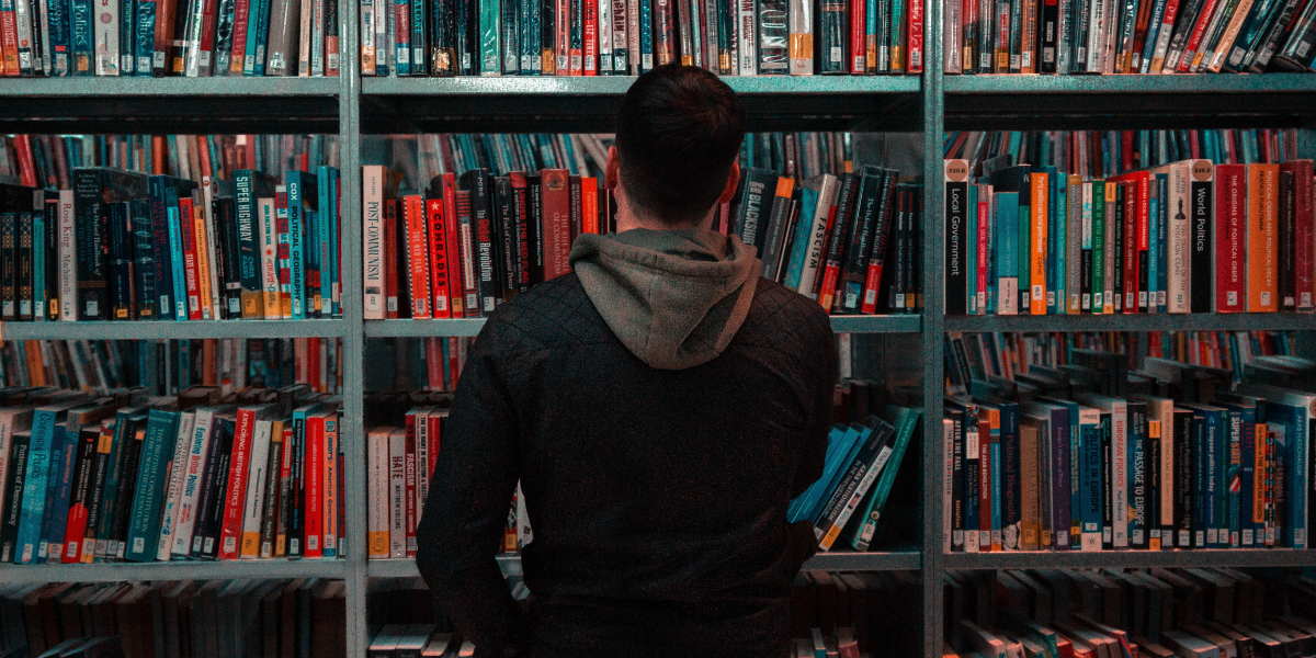 Man with his back turned to the camera looking at shelves filled with books