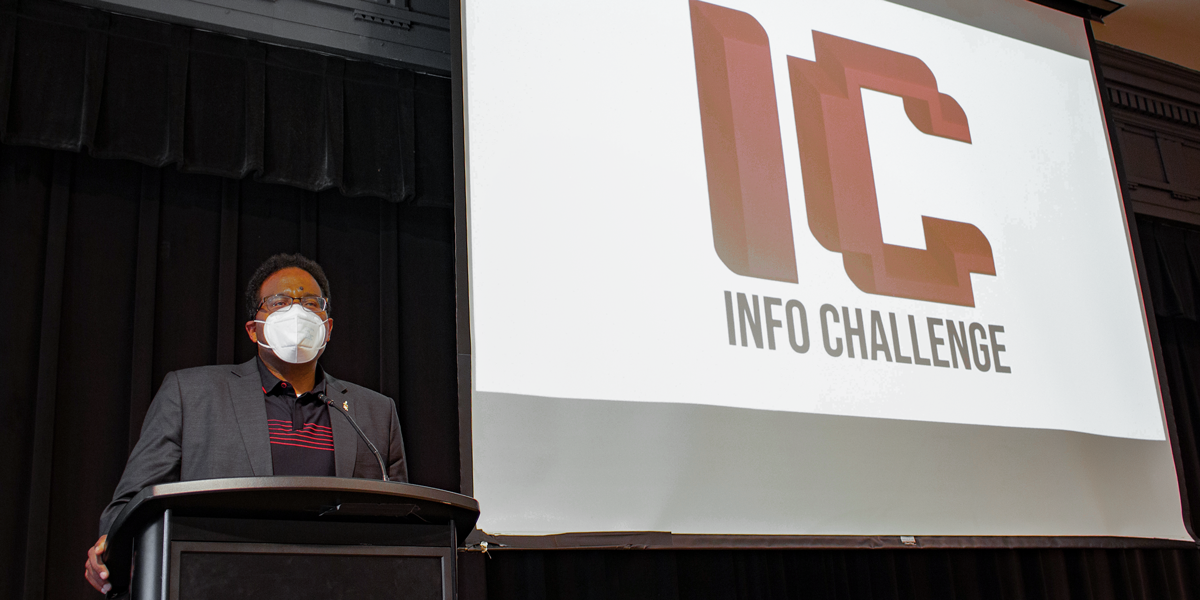 University of Maryland President Darryll Pines stands at a podium with the Info Challenge logo behind him on a projector