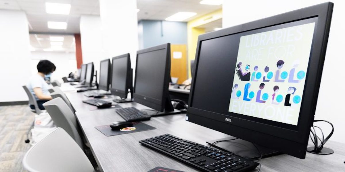 A computer lab with a student sitting in the background and a computer screen in the foreground that reads "Libraries are for everyone.