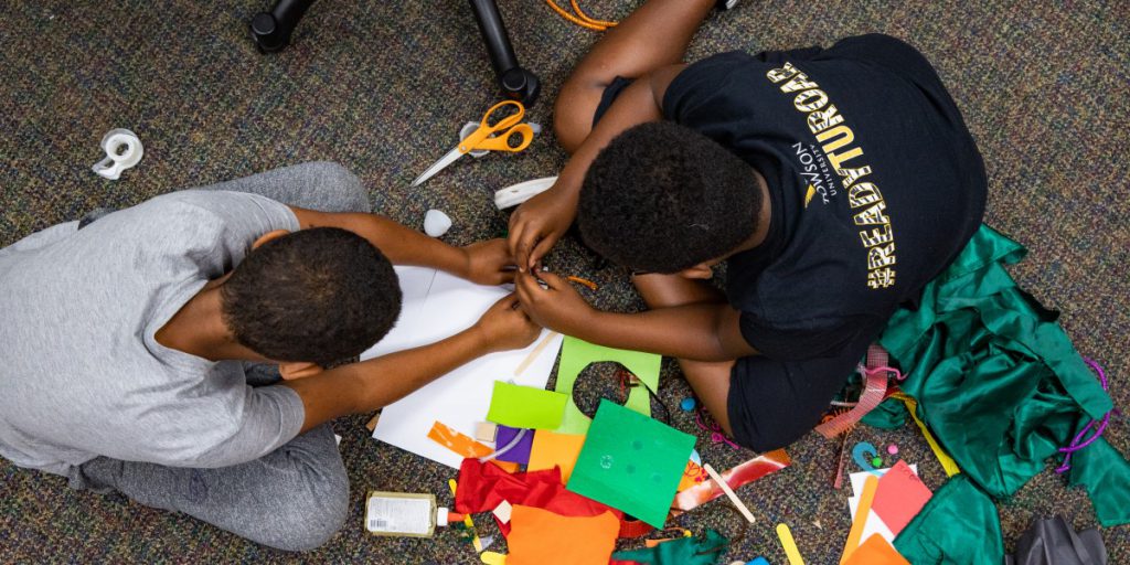 two young kids playing with fabric and paper on a carpeted floor