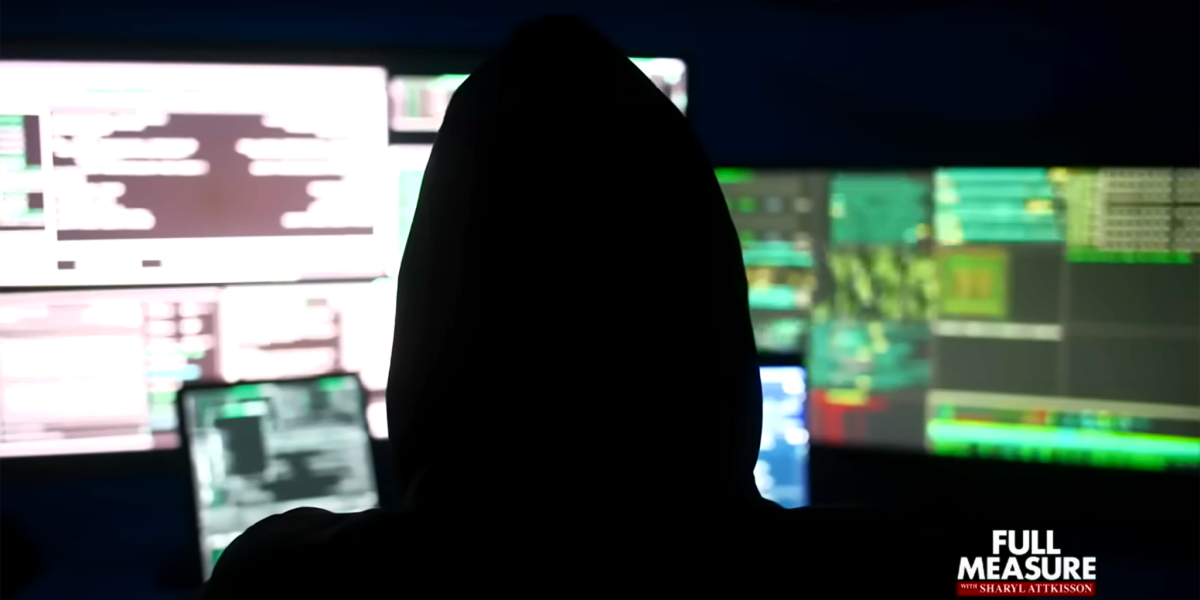 A silhouetted figure wearing a hood sits in the dark in front of a wall of glowing computer monitors. The screens display various lines of code, data, or technical interfaces in colors like green, red, and blue. The overall scene suggests a theme of hacking, cyber security, or covert operations. In the bottom right corner is a logo for "Full Measure with Sharyl Attkisson".