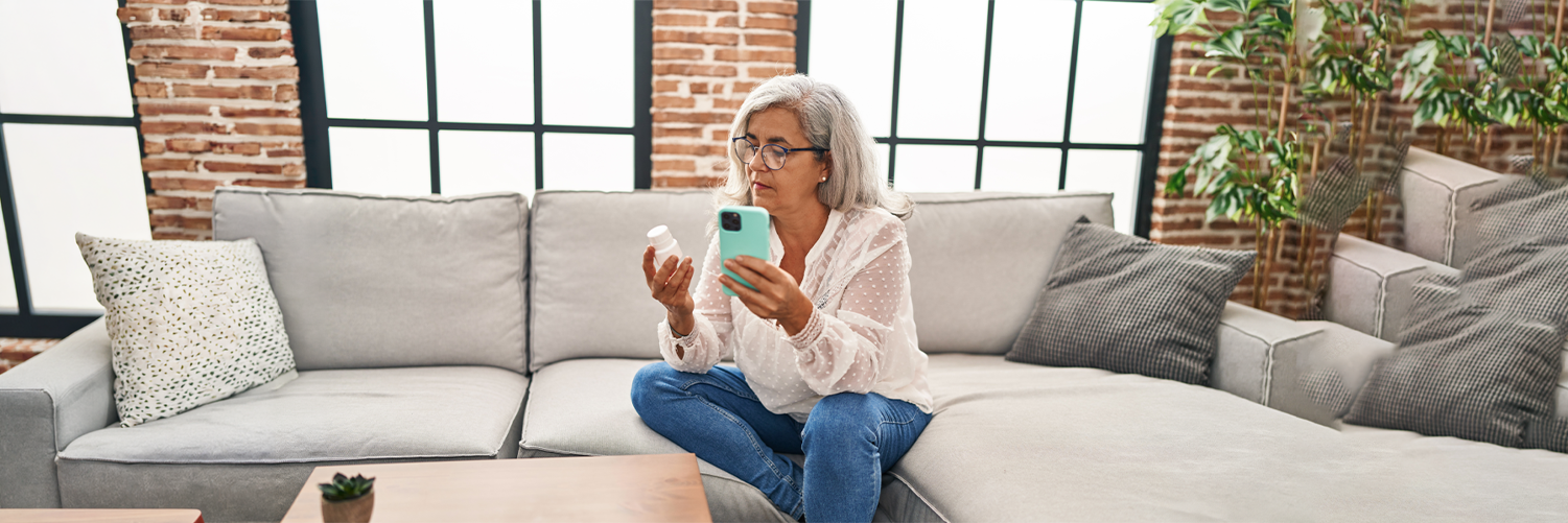 Middle age woman using smartphone holding pills at home