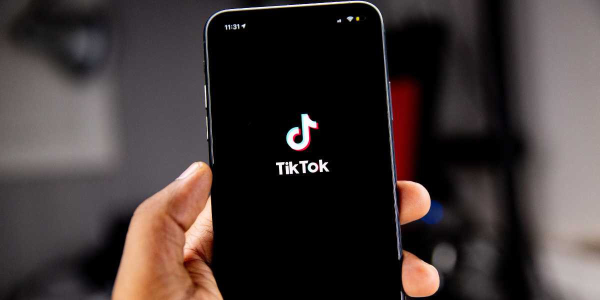 A hand holding up an iPhone with the TikTok logo displayed over a black background