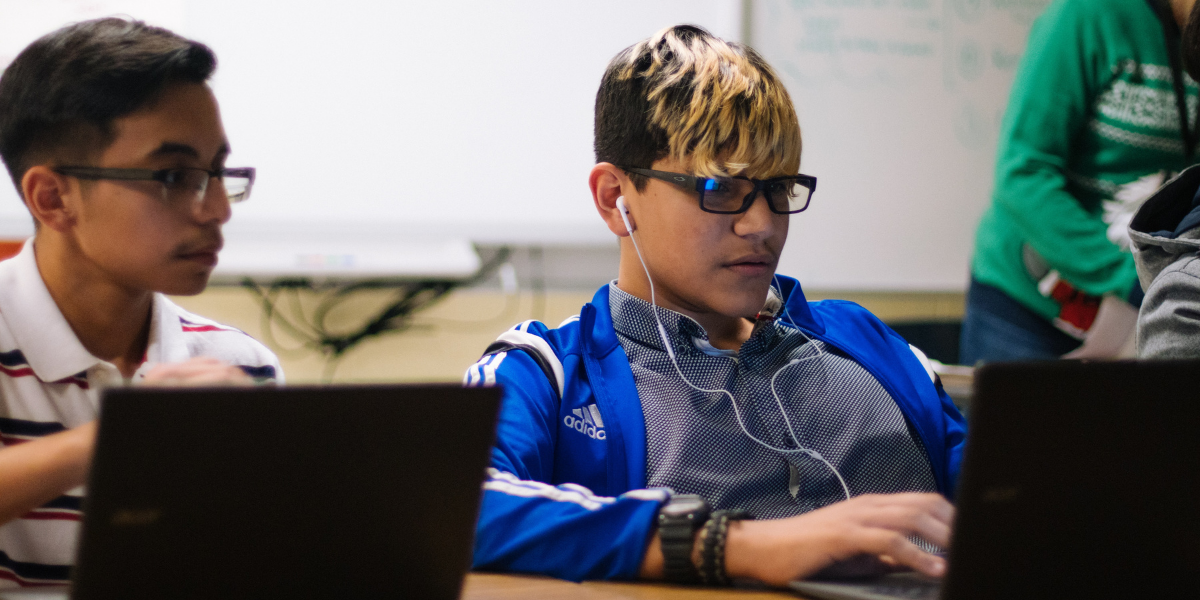 Two students sitting in front of laptops with the screen's reflection showing in their glasses