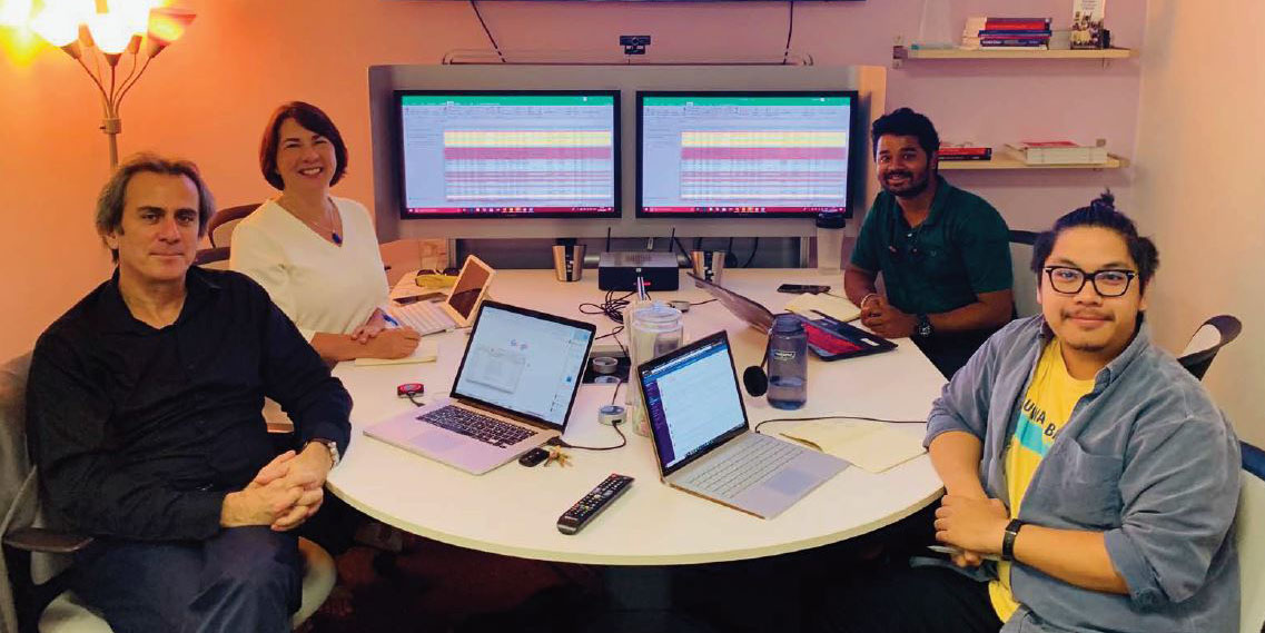 four people sitting around a table with laptops on them