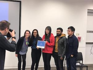 five people standing next to each other in front of a photographer holding a piece of paper up