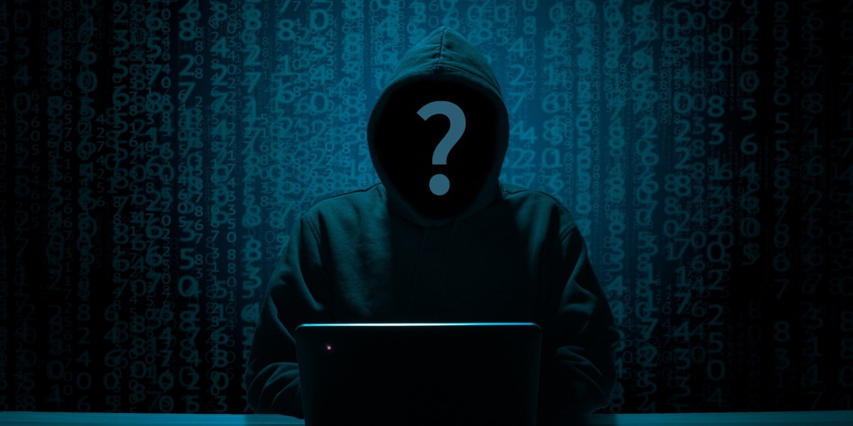 darrk image of person in a hooded sweatshirt in front of a laptop