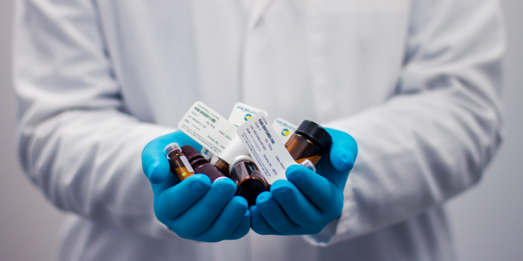 photo of person in a white coat and blue gloves holding vials