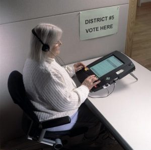 A person in a chair with her hands on A modern voting machine with EZ Access® 2