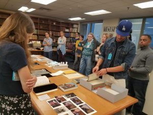 people standing around a room with a table in the center with books and paper on it