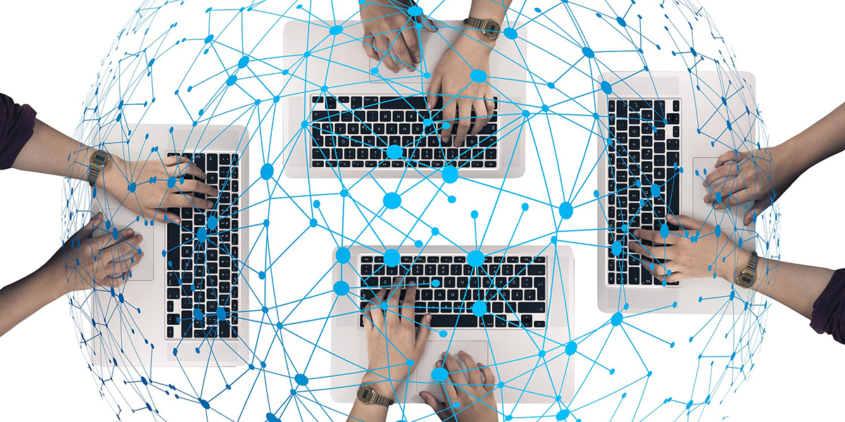 An aerial view of four people working on laptops with an illustrated network overlay