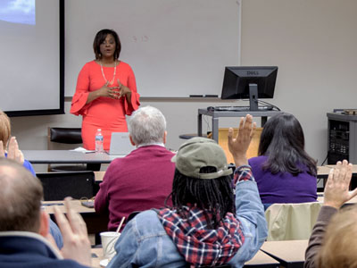 Dr. Nicol Turner Lee in front of seated people with their hands raised