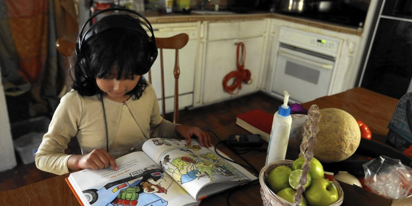 child with headphones on reading a book