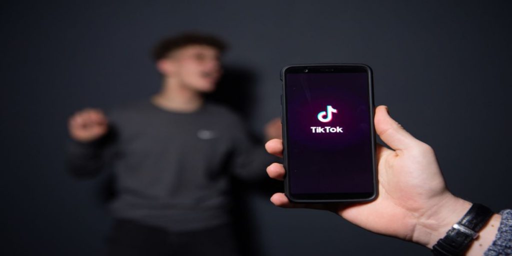 photo of tik Tok logo on a phone screen and an out of focus person standing in front of the phone